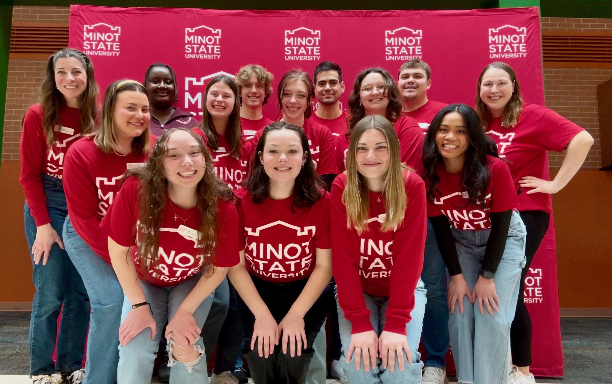 Group of Tour Guides posing in front of a Minot State backdrop